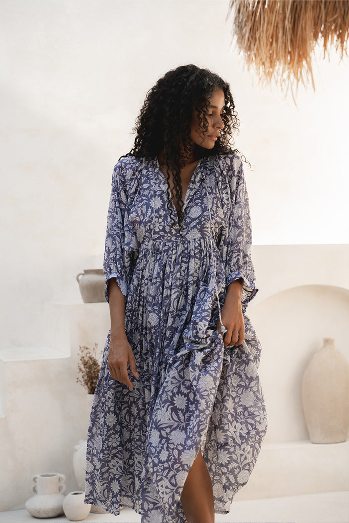 Kyra Midi Dress Blue Iris — lifestyle shot by white wall, front tie V-neck, hand block print cotton | Daughters of India