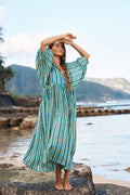 Woman standing on rocks by the sea wearing the Daughters of India Kyra Midi Dress in Spearmint, a flowing green striped cotton midi dress with billowed sleeves