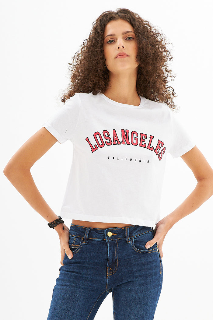 Model in L.A. Vibes white crop top with red Los Angeles graphic and high-waisted dark wash jeans streetwear.
