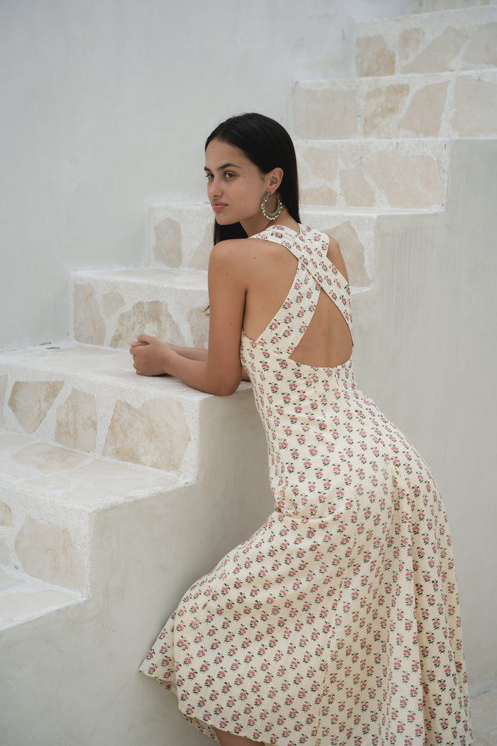 Lalika Dress Peony — lifestyle shot standing in European street, peony hand block print cotton wrap dress, cream with pink floral motifs, Mediterranean coastal village | Daughters of India