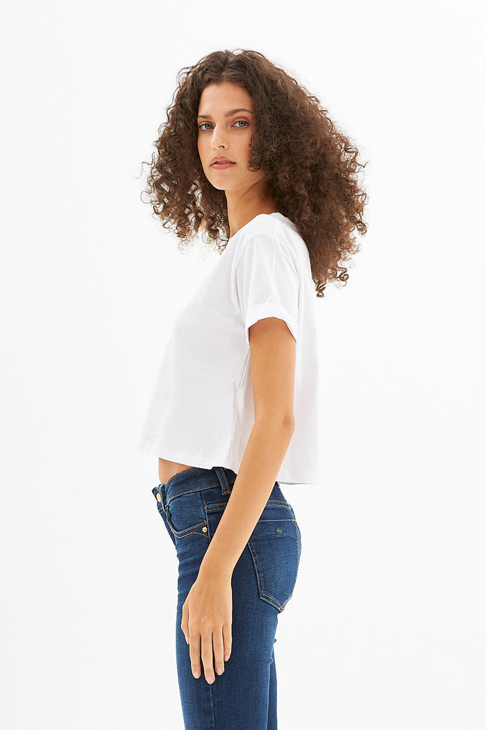 Side view of the Leah White Ribbed Crop Top paired with dark wash jeans on a model with curly hair.