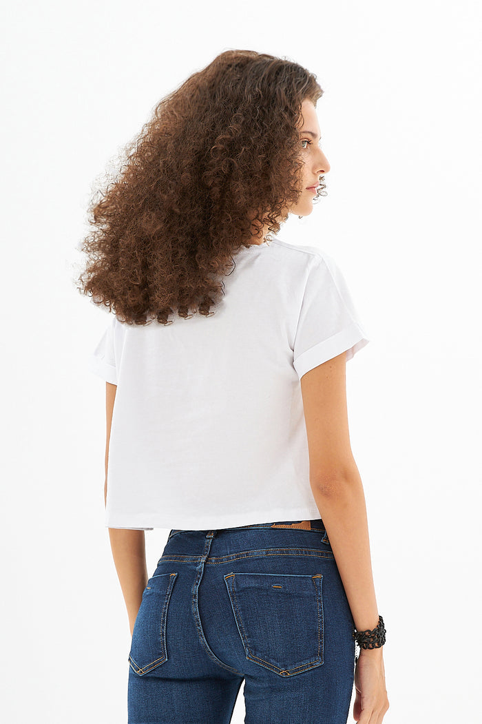 Back view of the white Leah Ribbed Crop Top with cuffed sleeves, paired with high-waisted blue jeans.
