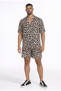 A man stands confidently in a short-sleeve, leopard print shirt and matching shorts, paired with black sneakers.