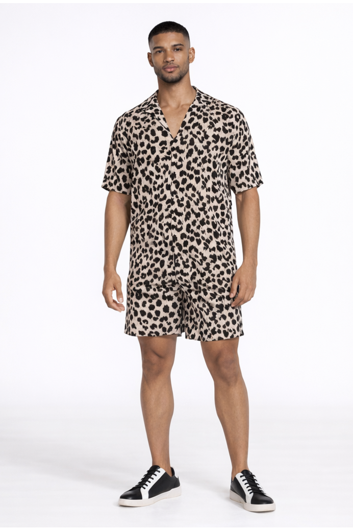 A man stands confidently in a short-sleeve, leopard print shirt and matching shorts, paired with black sneakers.