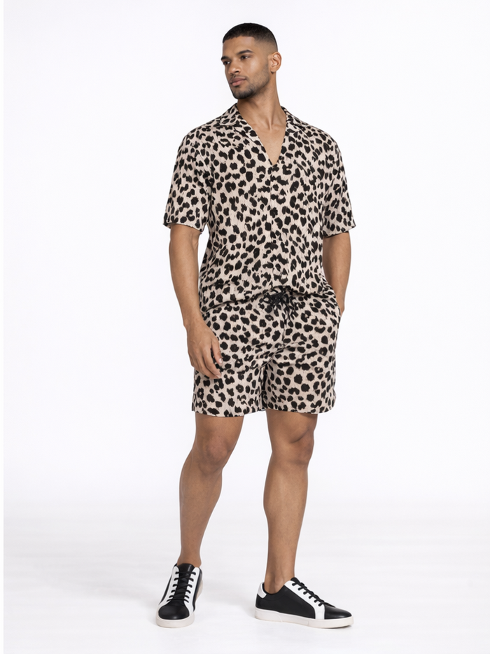A man stands confidently in a short-sleeve, leopard print shirt and matching shorts, paired with black and white snea...