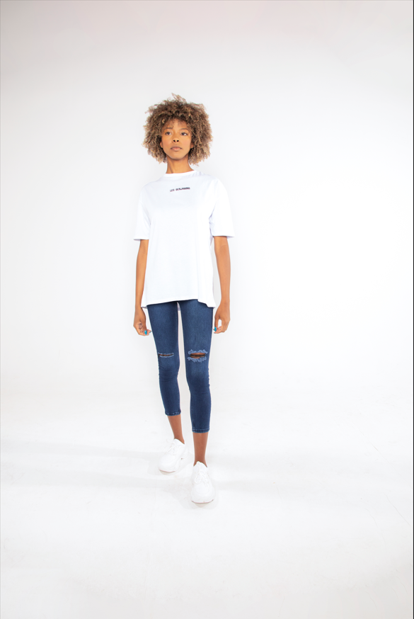 Model wearing a Les Benjamin white oversized streetwear graphic tee with logo on chest and distressed blue jeans.