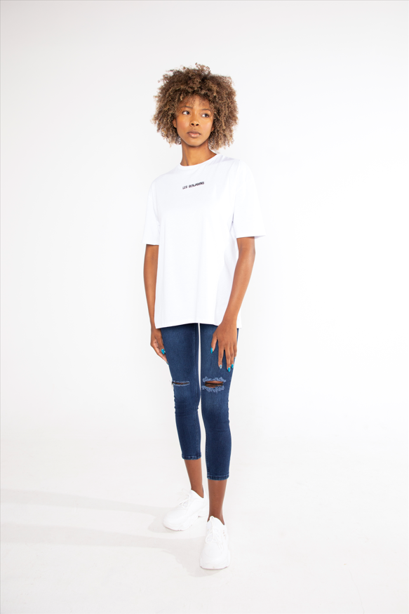 Model wearing a white Les Benjamins oversized streetwear graphic tee with dark distressed skinny jeans and sneakers.