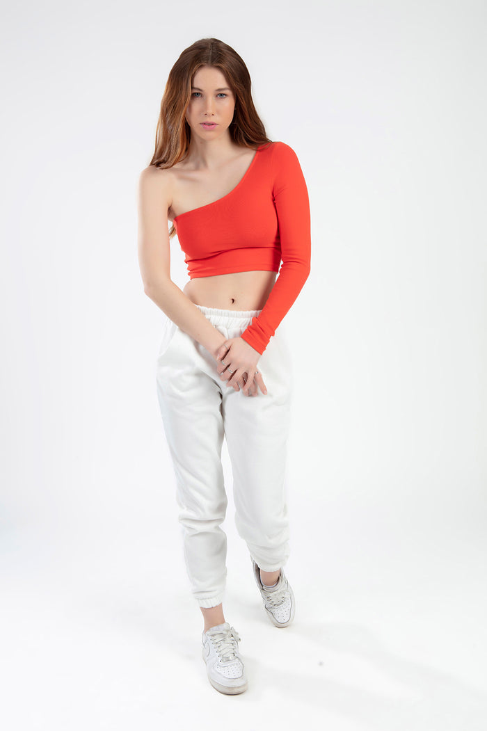 Model wearing the Lexie orange one-shoulder ribbed crop top with white joggers and sneakers.