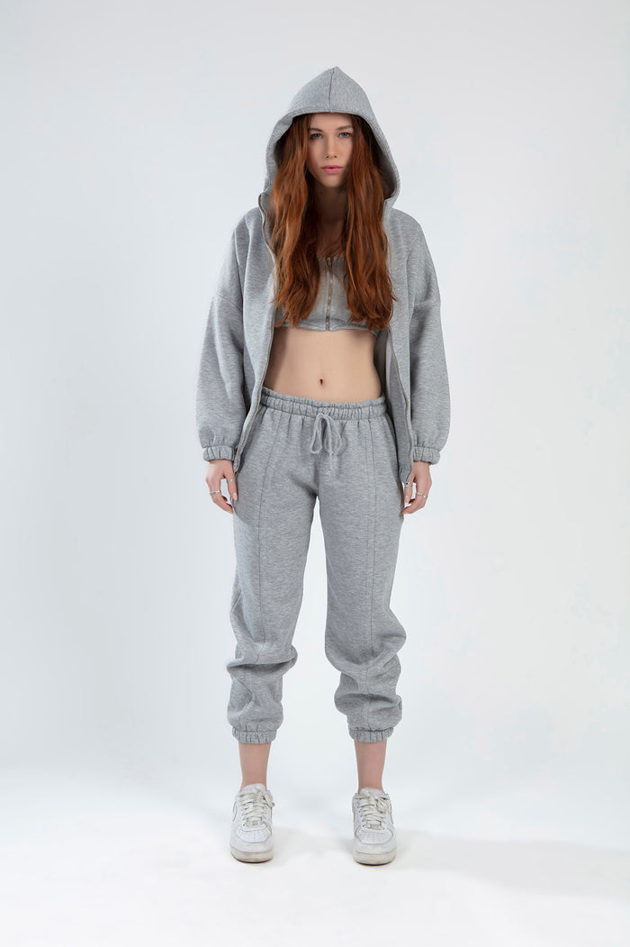 Model wearing Lily light grey matching jacket set with hooded zip-up, crop top, and drawstring joggers.