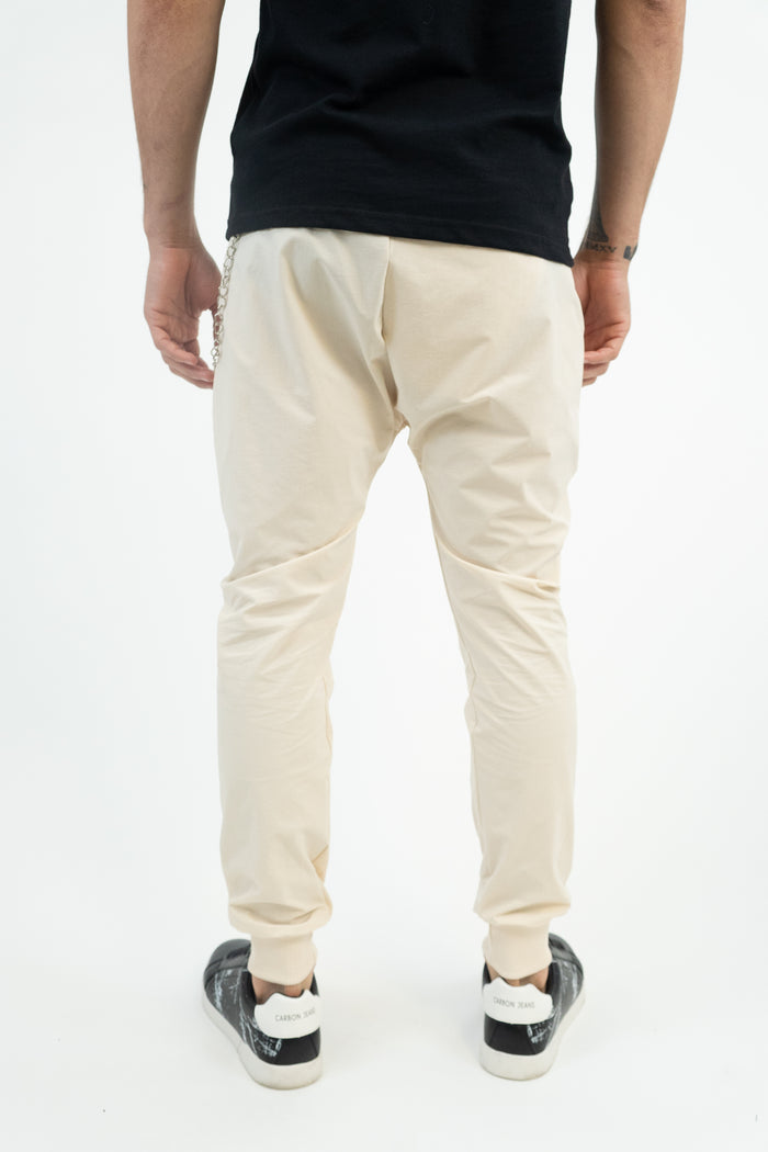 Back view of MAC cream slim-fit streetwear jogger pants with cuffed ankles and a silver hip chain detail.