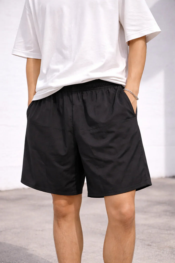 Man wearing black casual shorts with elastic waistband and white t-shirt outdoors