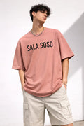 Man in pink graphic t-shirt with 'SALA SOSO' text and beige cargo shorts, casual style