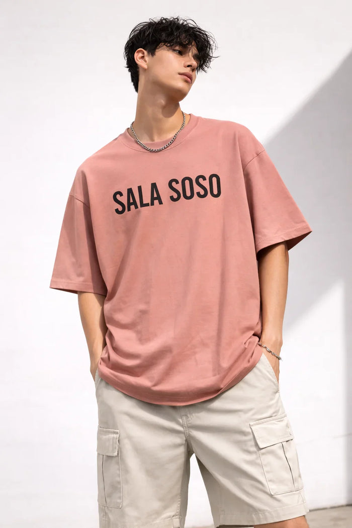 Man in pink graphic t-shirt with 'SALA SOSO' text and beige cargo shorts, casual style