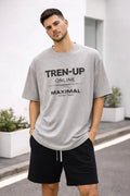 Man wearing a grey graphic T-shirt with 'TREN-UP ONLINE MAXIMAL' text and black shorts outdoors