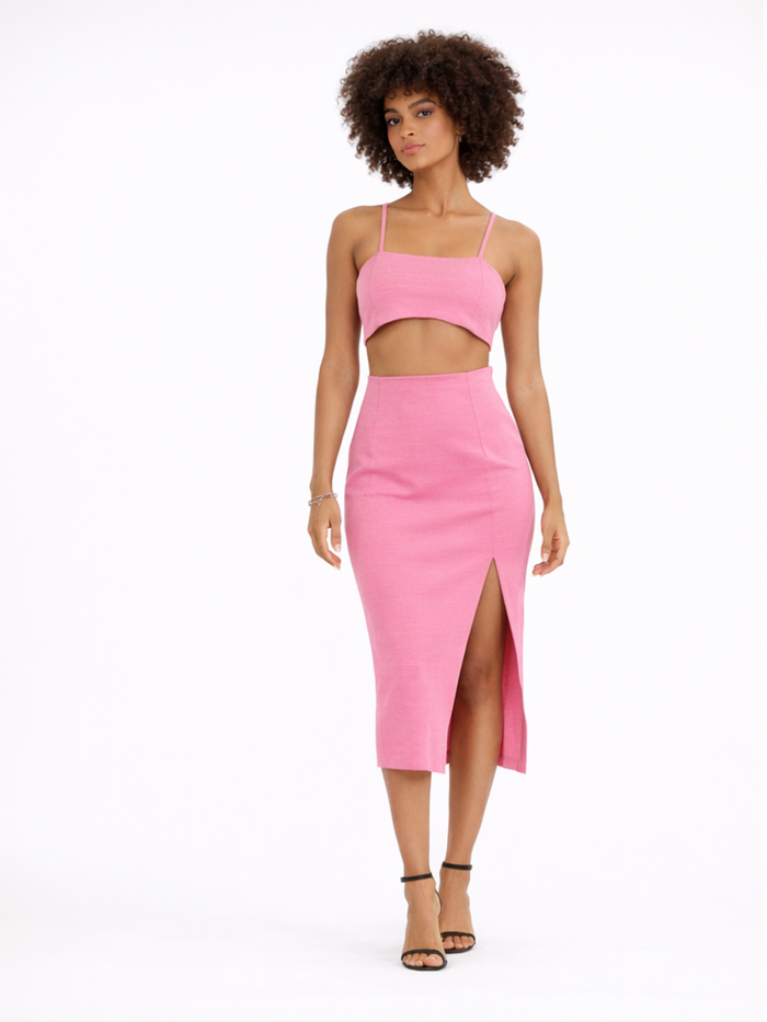 A model poses in a pink two-piece outfit featuring a cropped top and a midi skirt with a side slit.