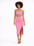 A model poses in a pink two-piece outfit featuring a cropped top and a midi skirt with a side slit.