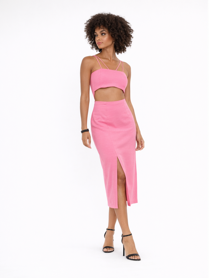 A model poses in a pink two-piece outfit featuring a cropped top and a midi skirt with a side slit.