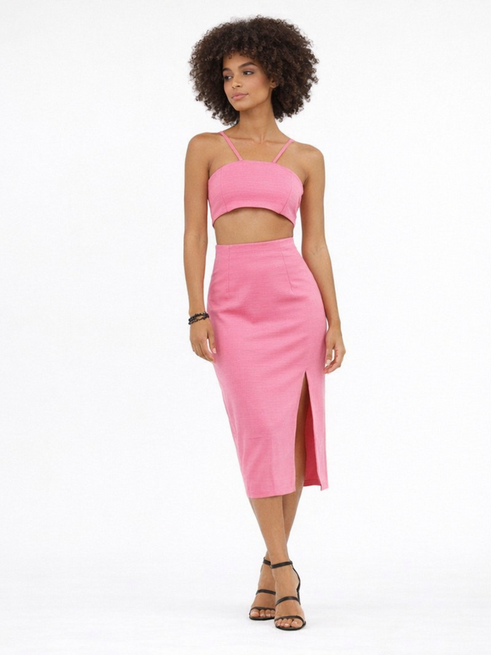 A model poses in a pink two-piece outfit featuring a cropped top and a midi skirt with a side slit.