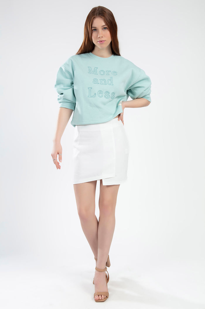 Model wearing the More and Less teal knit cropped sweatshirt and a white mini skirt against a white background.
