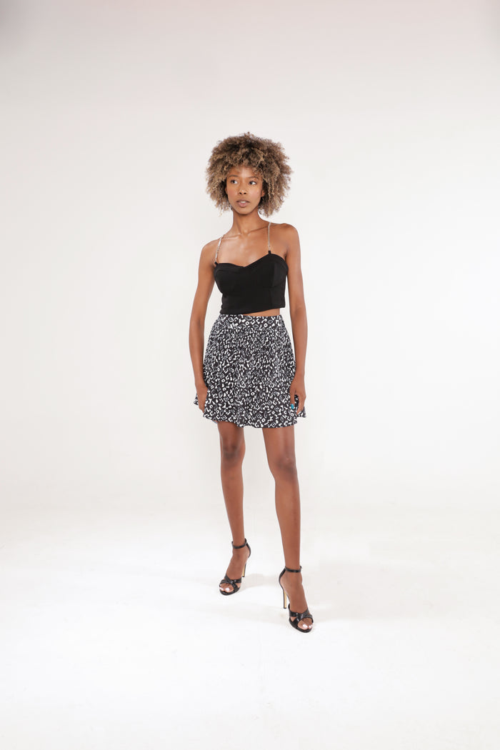 Model in Nika black sleeveless crop top with silver chain straps and a patterned mini skirt.