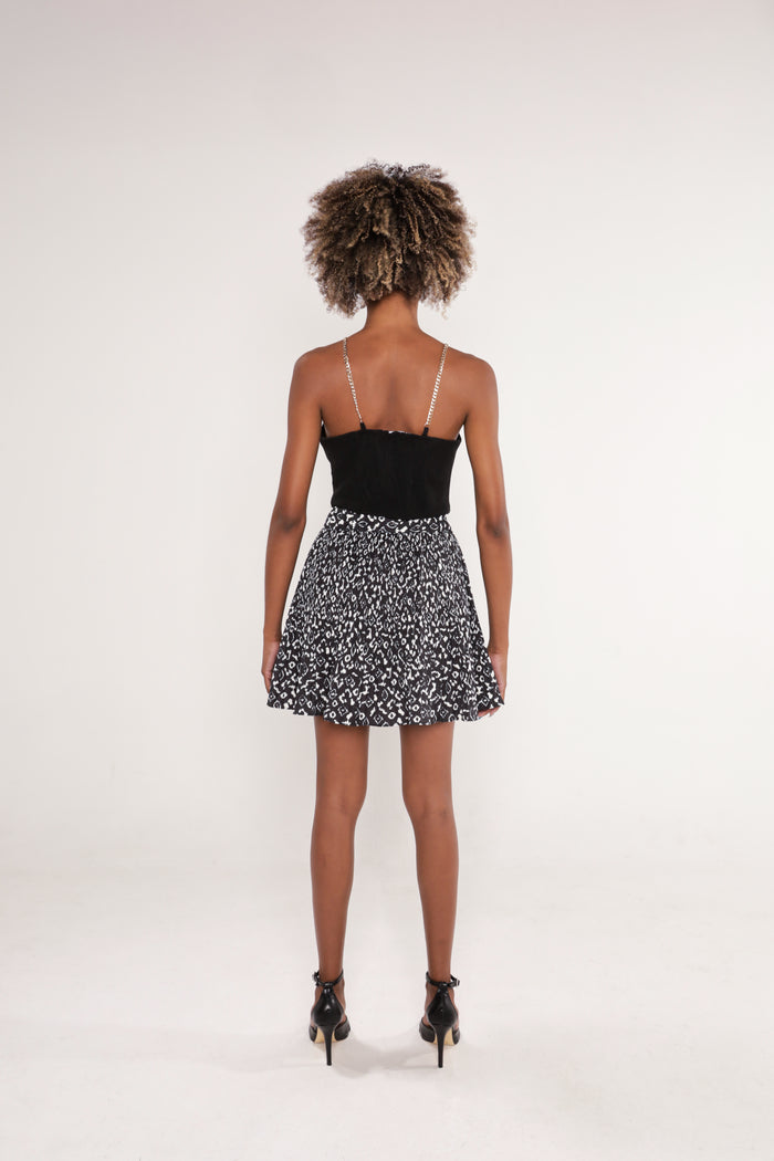 Back view of the Nika black sleeveless crop top with silver chain straps, paired with a patterned black and white mini skirt.