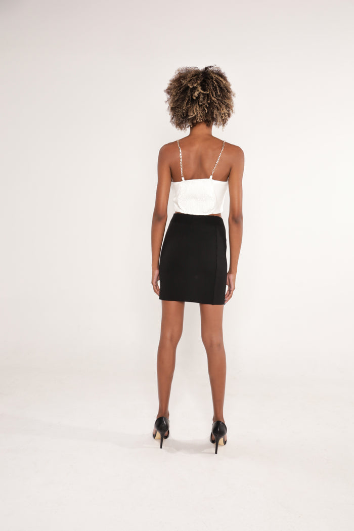 Back view of the Nika white crop top with silver chain straps and smocked detailing paired with a black mini skirt.