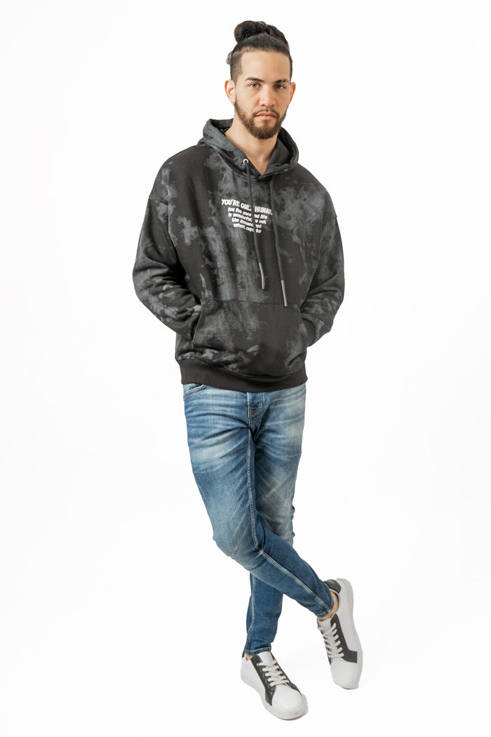 Model wearing Only Human black and grey tie-dye oversized graphic streetwear hoodie with blue jeans and white sneakers.