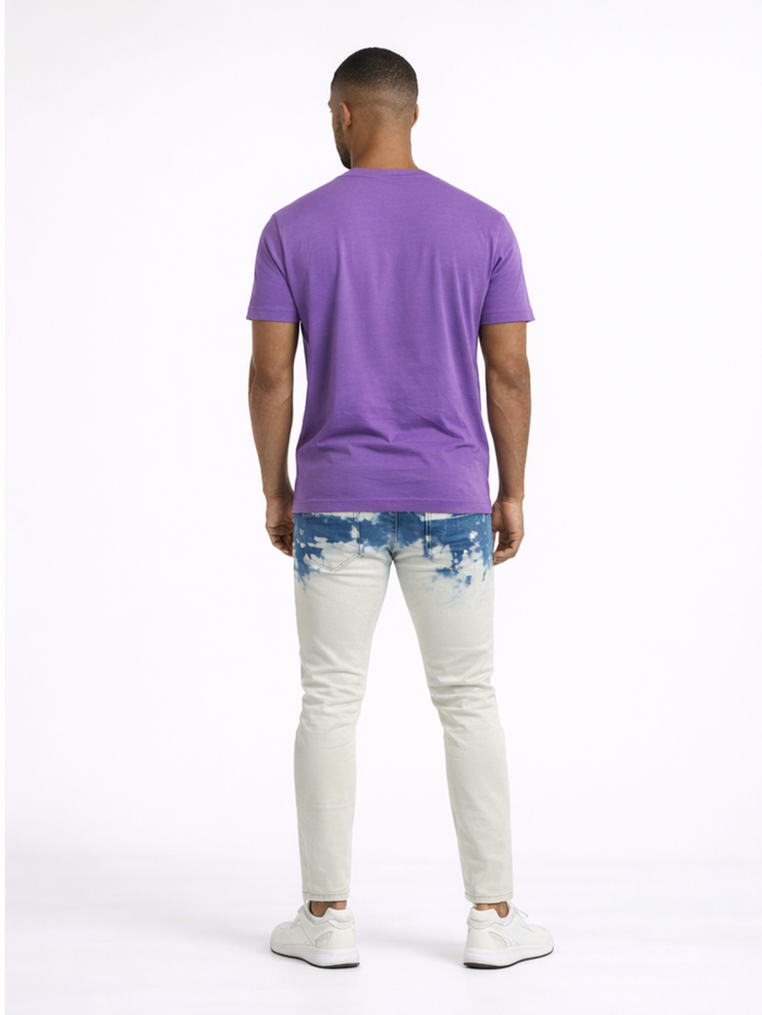 A person wearing a purple t-shirt and light-colored jeans with a blue tie-dye pattern, viewed from behind.