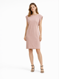 A woman stands in a relaxed-fit, short-sleeve pink dress paired with black strappy heels against a white background.
