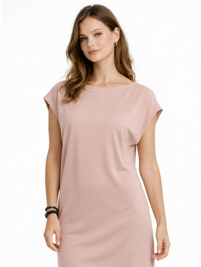 A woman with wavy hair wears a soft pink, short-sleeved dress, showcasing a relaxed fit and minimalistic design.