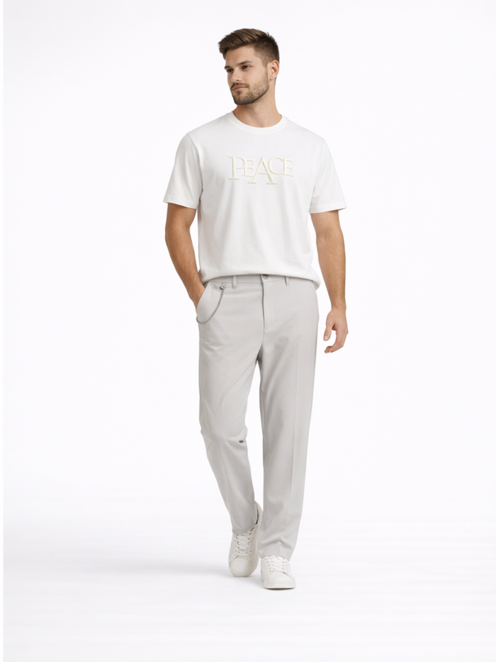 A man stands confidently in a white t-shirt with a textured "PEACE" graphic, paired with light gray pants and white s...