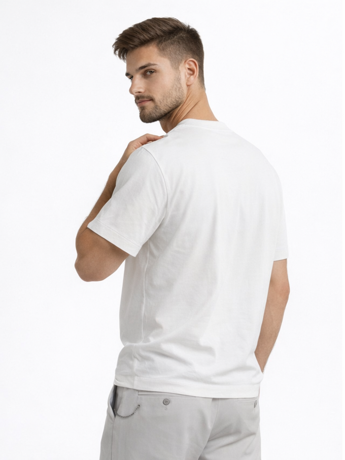 A young man with short hair wearing a plain white t-shirt, looking back over his shoulder against a light background.