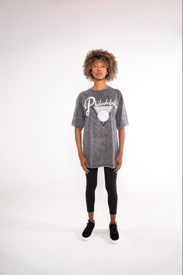 Model wearing an oversized Philadelphia acid wash graphic tee in grey with black leggings and sneakers.