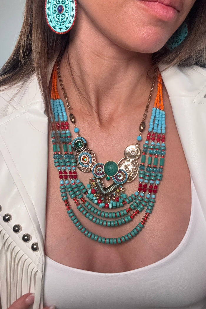 Piper Necklace featuring multi-strand turquoise beads, gold accents, warm red and orange detailing, and a sculptural pendant centerpiece.