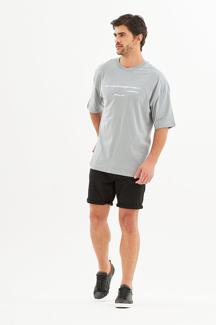 Model in the Popit Grey Oversized Shirt with white chest text, black streetwear shorts, and black sneakers.
