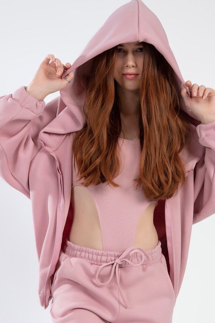 Model wearing the salmon pink Remi Jacket Set featuring a hooded zip-up, cut-out bodysuit, and matching joggers.