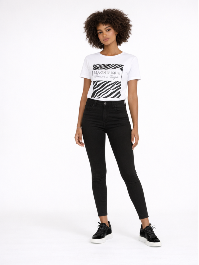 A model stands confidently in a graphic tee and black skinny jeans, paired with stylish black sneakers.