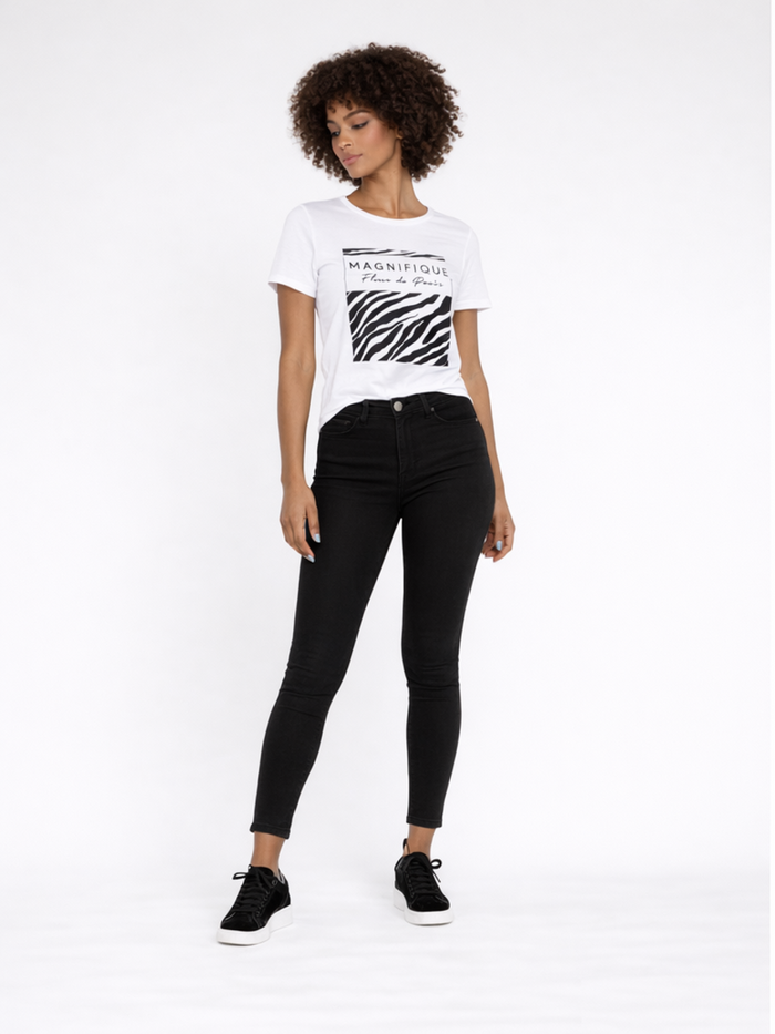 A model poses in a white graphic t-shirt and black skinny jeans, paired with black sneakers.