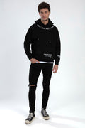 Man in black hoodie with 'Worry Less' embroidery, distressed skinny jeans, and high-top sneakers streetwear outfit.