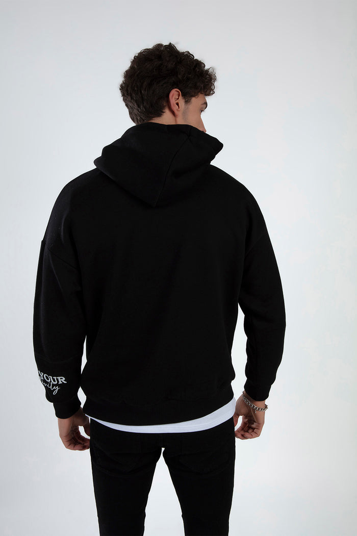 Back view of a man wearing a black streetwear hoodie with white embroidery on the sleeve and a relaxed fit.