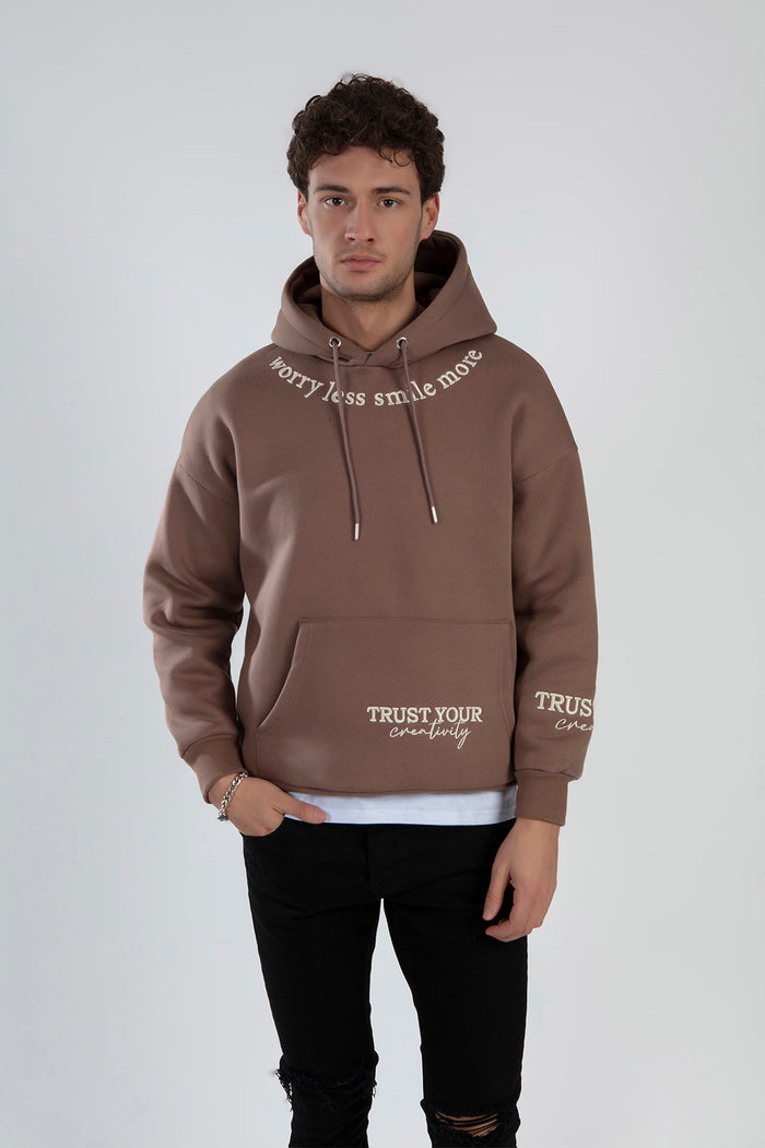 Man in a brown graphic hoodie with Worry Less Smile More embroidery and Trust Your Creativity streetwear design.
