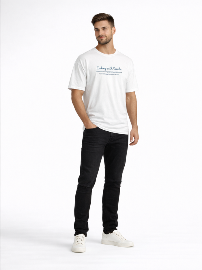 A man stands confidently in black jeans and a white t-shirt, paired with white sneakers.