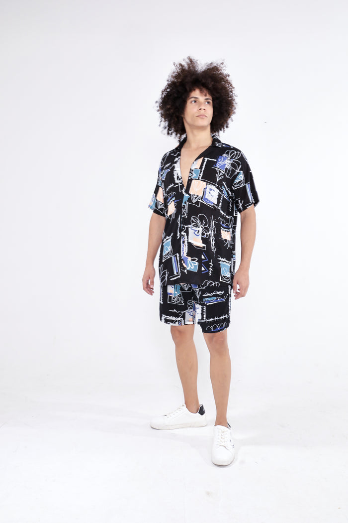 Man in Ryland two-piece matching set with black short-sleeve button-down shirt and shorts in abstract streetwear print.