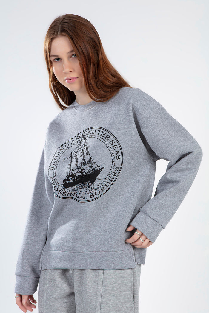Model wearing an oversized light grey streetwear sweatshirt with a black circular nautical sailing ship graphic.
