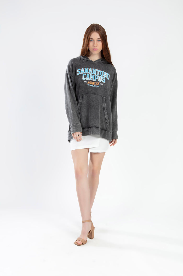 Model in Sanatond Campus grey washed oversized hoodie with a graphic print, white mini skirt, and tan heels.