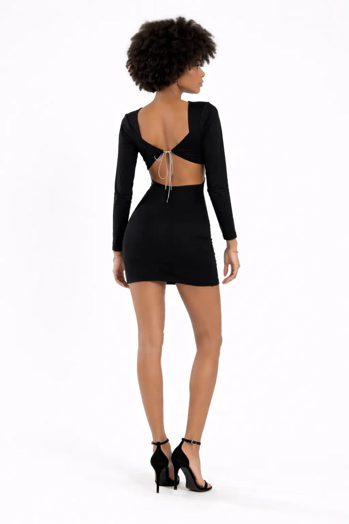 A model showcases a fitted black dress with long sleeves and an open back, paired with black high-heeled sandals.