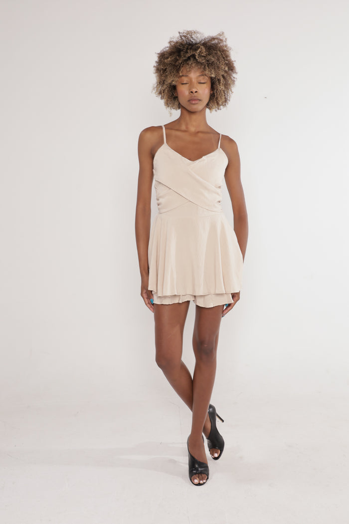 Model wearing the Scarlet Romper, a beige summer one-piece with crossover bodice and thin straps.