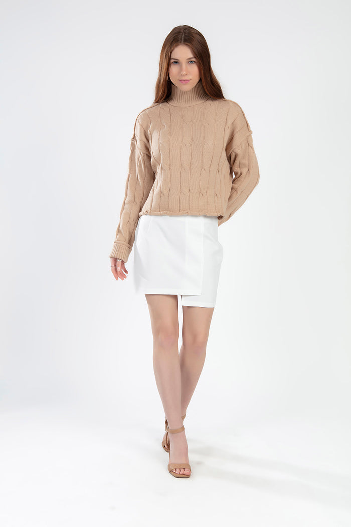 Serena beige cable knit turtleneck sweater in an oversized fit paired with a white mini skirt.