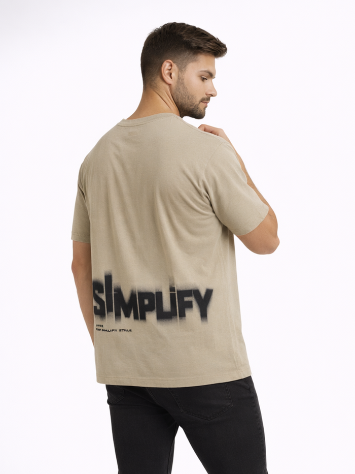 A man wearing a beige t-shirt with a large black spray-painted text design on the back.