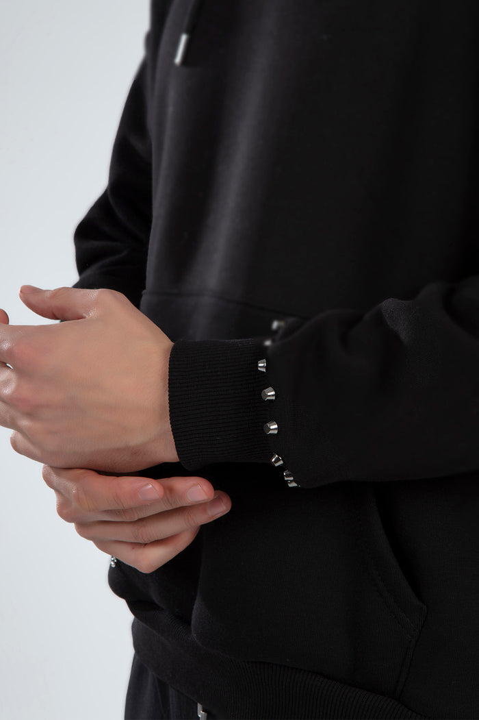 Detail of silver metal studs on the ribbed cuff of a black oversized Carbon streetwear hoodie for a hype vibe.